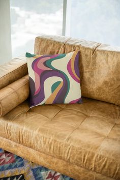 a brown leather chair with a colorful pillow on it's back and a window in the background