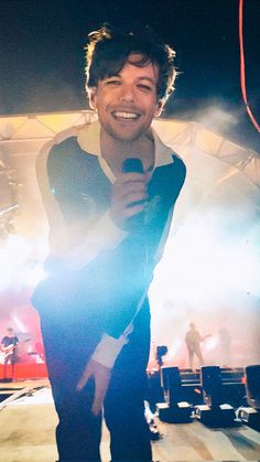 a smiling man holding a microphone in front of a stage with other people on it