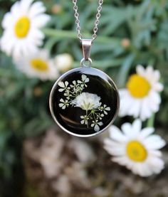 a necklace with white flowers on it is hanging from a chain in front of some daisies