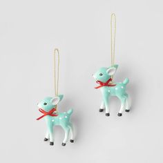 two christmas ornaments hanging from strings on a white surface, one with a deer ornament and the other has a red ribbon around it's neck