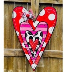 a heart shaped door hanger hanging on a wooden fence with polka dots and hearts painted on it