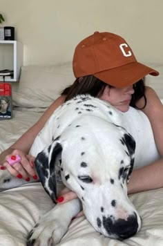 a woman laying on top of a bed with a dalmatian dog wearing a hat