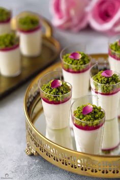 small cups filled with green and white desserts on a gold serving tray next to pink flowers