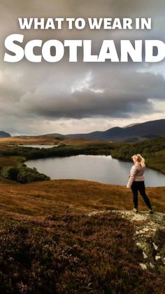 a woman standing on top of a hill next to a lake