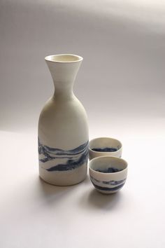 a white and blue vase sitting next to two bowls on top of a table in front of a white background