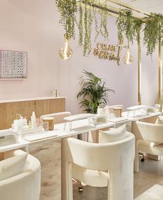 the interior of a nail salon with white chairs and plants hanging from the ceiling above