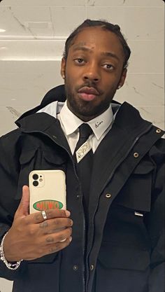 a man in a black jacket is holding a cell phone and looking at the camera