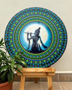 a decorative plate sitting on top of a wooden stool next to a potted plant