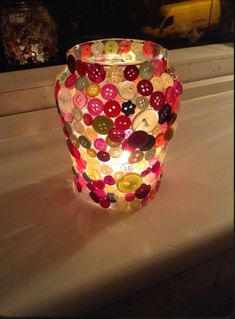 a glass vase with buttons on it sitting on a table next to a candle holder