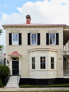 a large white house with black shutters on the front and side windows, next to a green lawn