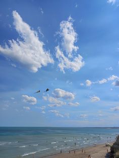 several people are on the beach and one is flying a kite in the blue sky