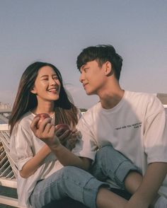 a man and woman sitting on top of a bench next to each other holding apples