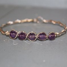 Five juicy purple genuine amethyst beads in a sterling silver wirewrapped bracelet. Lightweight, stackable, fun to wear, in a color everyone loves! Amethyst is the birthstone for those born in February, so this would make a nice affordable gift! Or treat yourself--it will go great with an armful of other bangles! Purple has long been the color of royalty, and amethyst is said to bring the wearer good luck and protection against drunkenness! Choose from the size variations for a perfect custom fi Purple Beaded Bracelets, Amethyst Bracelet Beads, Born In February, Wire Jewelry Designs, Wire Bangles, Bead Bangles, Crystal Beads Bracelet, Amethyst Bracelet, February Birthstone