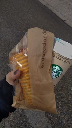 a person holding a bag of hotdogs and a cup of coffee on the street