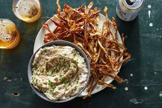 a plate full of fries and dip next to two beers