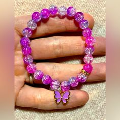 a woman's hand holding a pink bracelet with purple beads and a butterfly charm