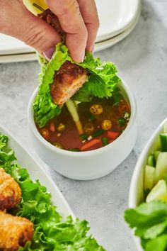 a person dipping some food into a bowl filled with lettuce and other vegetables