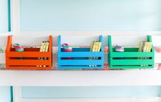 three colorful wooden crates sitting on top of a white shelf