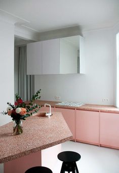 an empty kitchen with pink cabinets and stools next to the counter top, in front of a large mirror