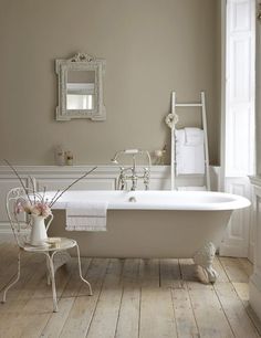 a white bath tub sitting in a bathroom next to a mirror and chair with flowers on it