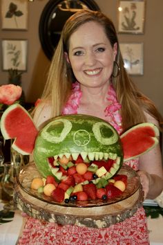 a woman holding up a watermelon carved to look like a face with fruit on it