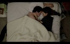 a man and woman laying in bed under the covers with their faces close to each other