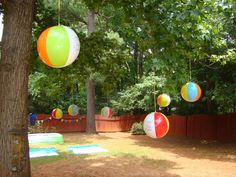 several colorful balls hanging from trees in a yard with other decorations on the fenced area