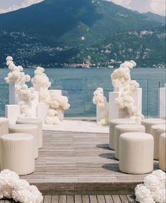 there are many white vases with flowers on the ground next to water and mountains in the background