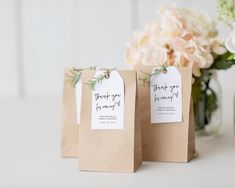 two small brown bags with tags on them sitting next to a vase filled with flowers