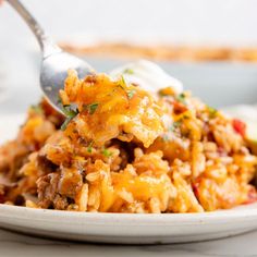 a white plate topped with rice covered in meat and vegetables next to a fork on top of it