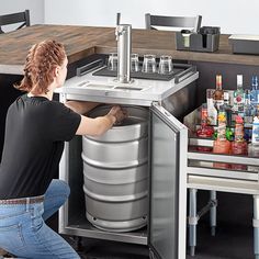 a woman is opening the bottom half of a stainless steel beverage dispenser