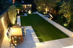 an outdoor dining area is lit up at night with lights on the walls and lawn