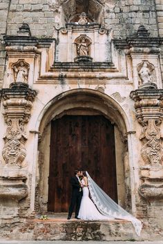 a man and woman standing in front of a wooden door with a wedding dress on