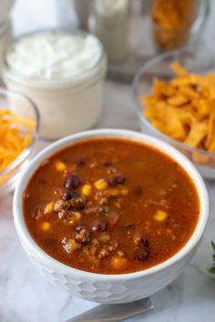 a white bowl filled with chili, cheese and tortilla chips on top of a table