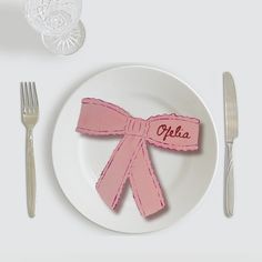 a white plate topped with a pink bow next to silverware and utensils