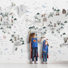 two young children standing in front of a wall with animals on it and the map of the world behind them