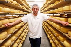 a man standing in front of stacks of cheeses with his hands out to the camera