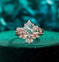 a green and white diamond ring sitting on top of a velvet covered cushioned surface