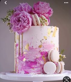 a pink and gold cake with flowers on the top is decorated with macaroons