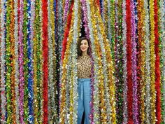 a woman standing in front of a wall covered with multicolored streamers and confetti