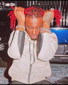 a man with red dreadlocks sitting in front of a car holding his hands to his head