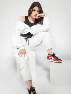 a woman sitting on top of a white box wearing red and black sneakers with her hand under her chin