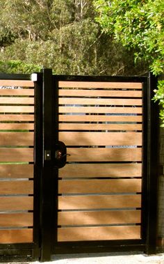 a wooden gate with two black gates on top of it and trees in the background