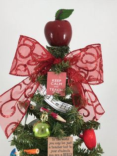 a christmas tree with an apple on top and red ribbon tied around the top, surrounded by other decorations