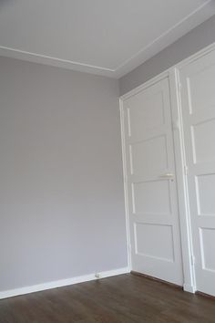 an empty room with two white doors and hard wood flooring on the far wall