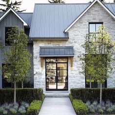 the front entrance to a house with hedges and trees on either side of the door