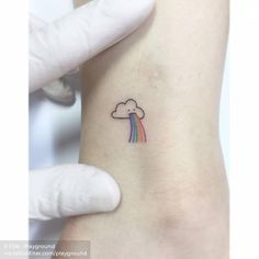 a small rainbow tattoo on the left side of the arm, with a cloud above it