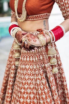 a woman wearing a red and gold lehenga with her hands on her hip