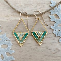 two pairs of gold and green beaded triangle earrings on a string with snowflakes in the background