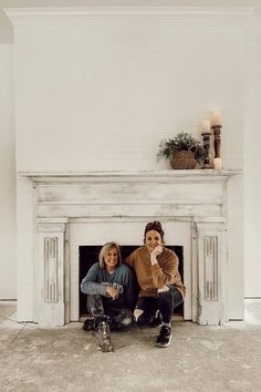 two women sitting on the floor in front of a fireplace